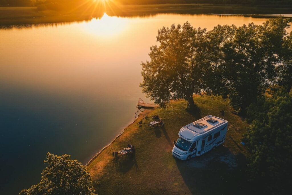 Campingplatz vs Stellplatz fuer Wohnmobile und Camper Wohnmobil steht am See bei Sonnenuntergang